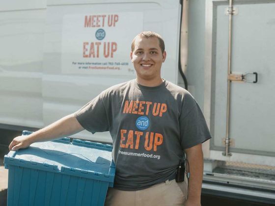 Alejandro holding a bin and standing in front of his delivery van.